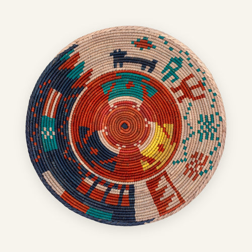 Ancient Lore Bold woven wicker wall basket with concentric geometric bands in beige, rust red, navy, teal, and yellow.