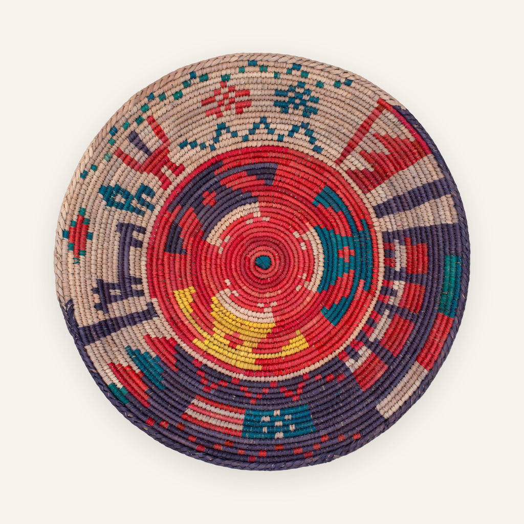 Ancient Lore Morganite handmade woven wicker wall basket with a red radial center, purple, teal blue, beige, and yellow geometric bands.