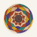 Canyon Prism woven wicker wall basket with a brown spiral center and concentric geometric bands in beige, rust red, yellow, green, and purple