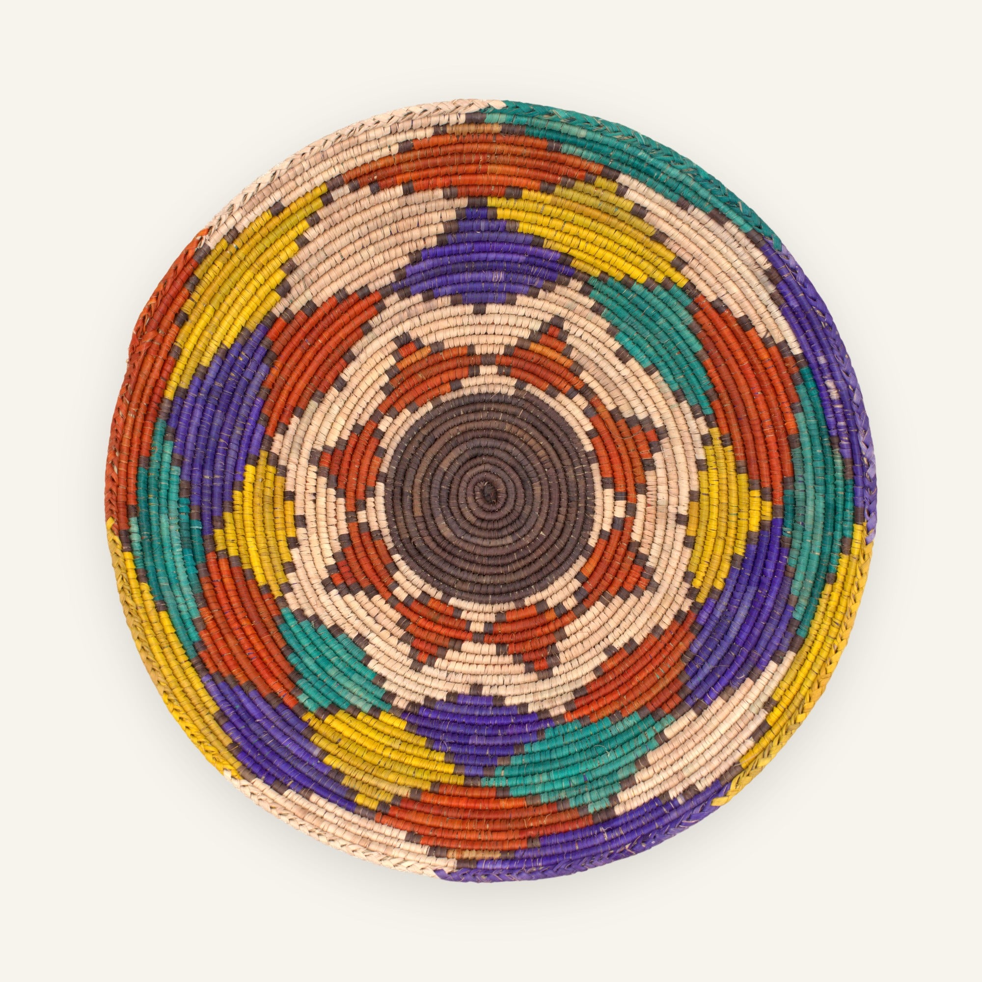 Canyon Prism woven wicker wall basket with a brown spiral center and concentric geometric bands in beige, rust red, yellow, green, and purple