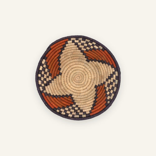 Ember Passage handmade woven wicker wall basket with a beige coiled center, orange curved bands, and dark geometric border.