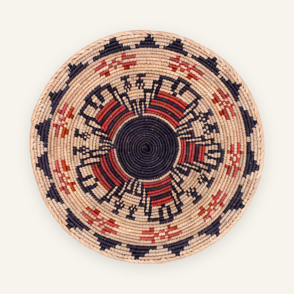 Mystery Garnet handmade woven wicker wall basket with a black center, beige ground, and red and orange geometric radial pattern.