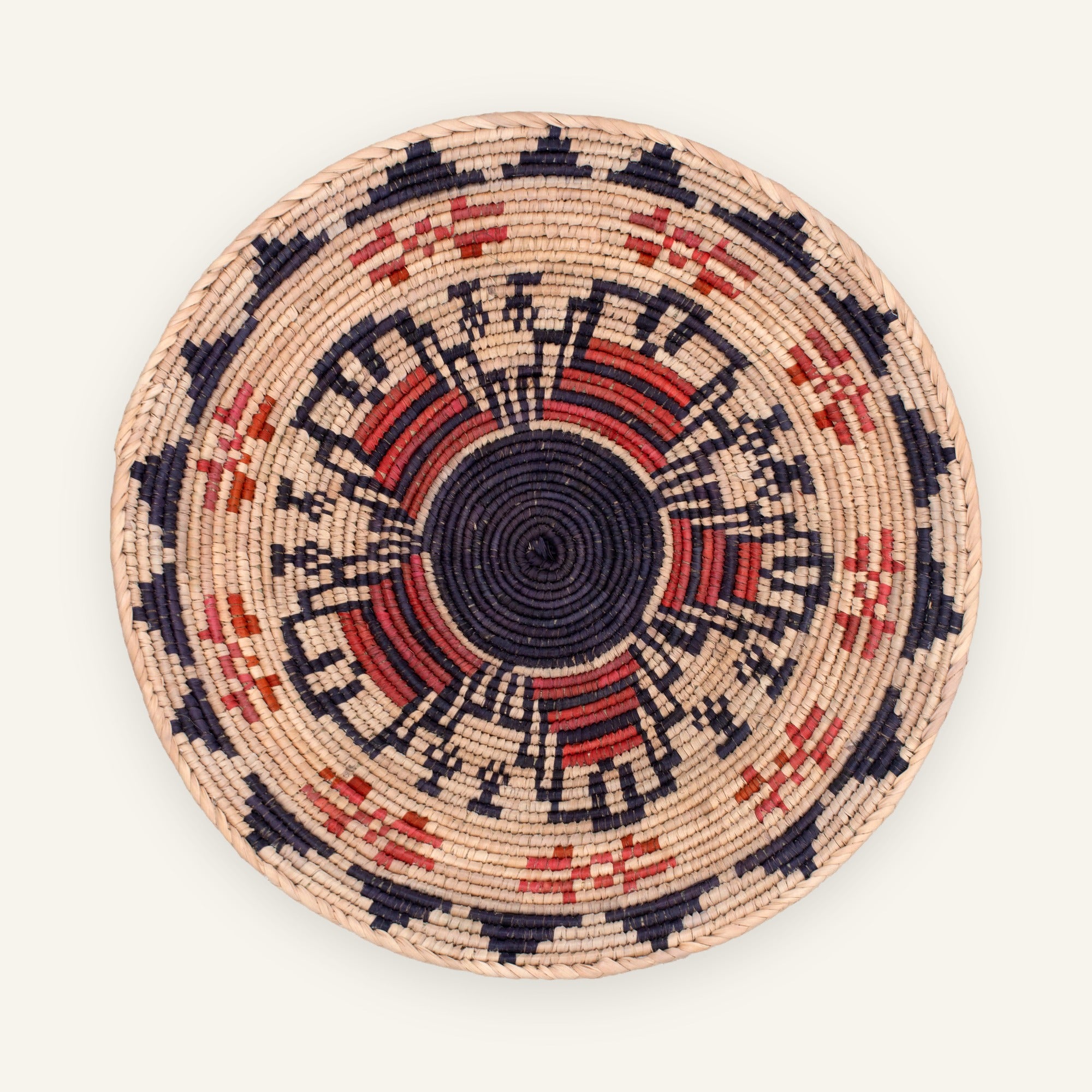 Mystery Garnet handmade woven wicker wall basket with a black center, beige ground, and red and orange geometric radial pattern.