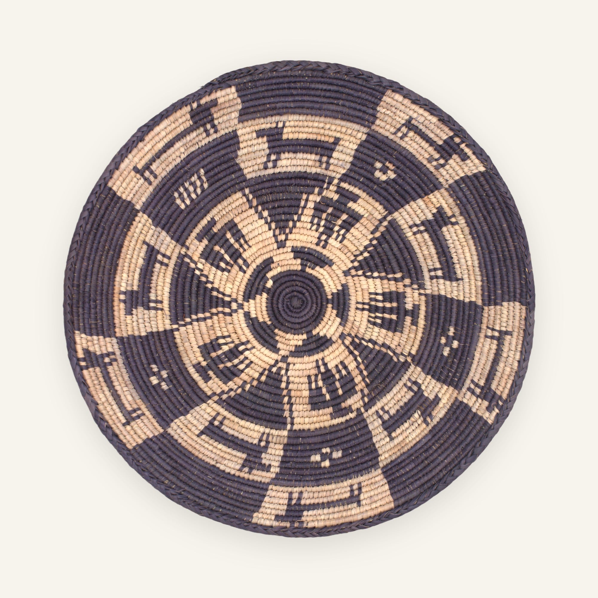 Society woven wicker wall basket in deep navy and natural beige with a radial geometric pattern