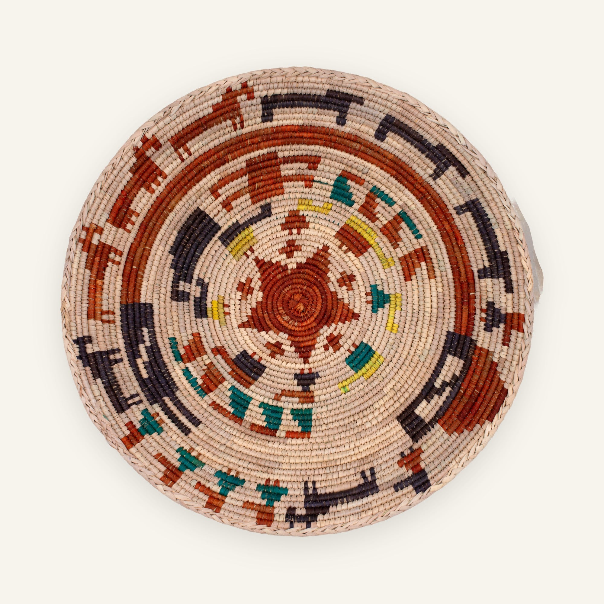 Stories Obsidian woven wicker wall basket with rust-red circular bands, dark arcs, teal details, and yellow accents on a natural beige ground.