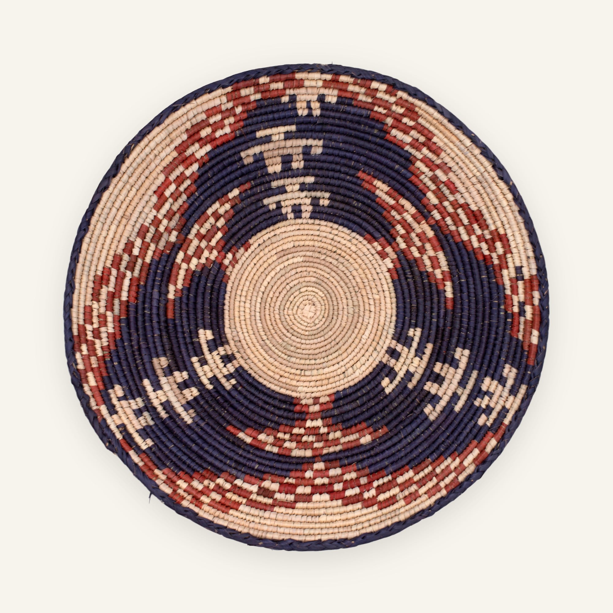 Visitors handmade woven wicker wall basket with a natural beige center, deep dark blue-black rings, and rust-red geometric arcs.